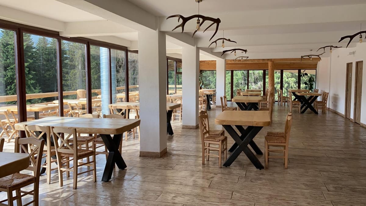 Interiorul restaurantului RâncaSki, cu mese din lemn și vedere spre pădure